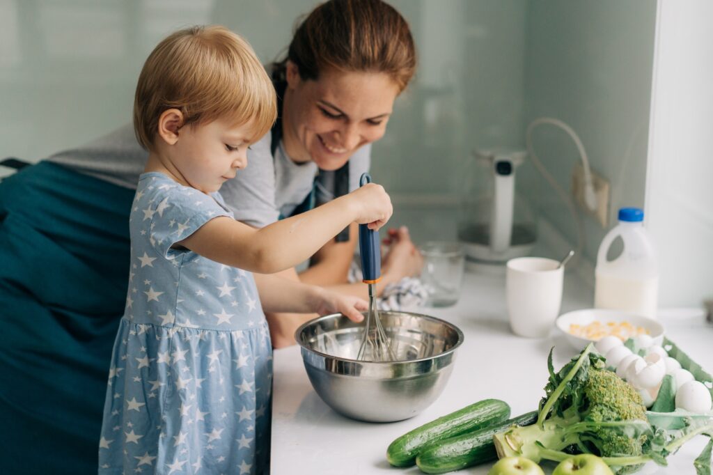 Toddler little daughter helps her mother cook an omelet.