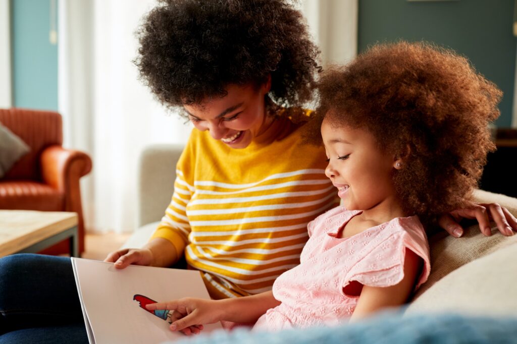 Mother And Daughter Relaxing On Sofa At Home Reading Book Together