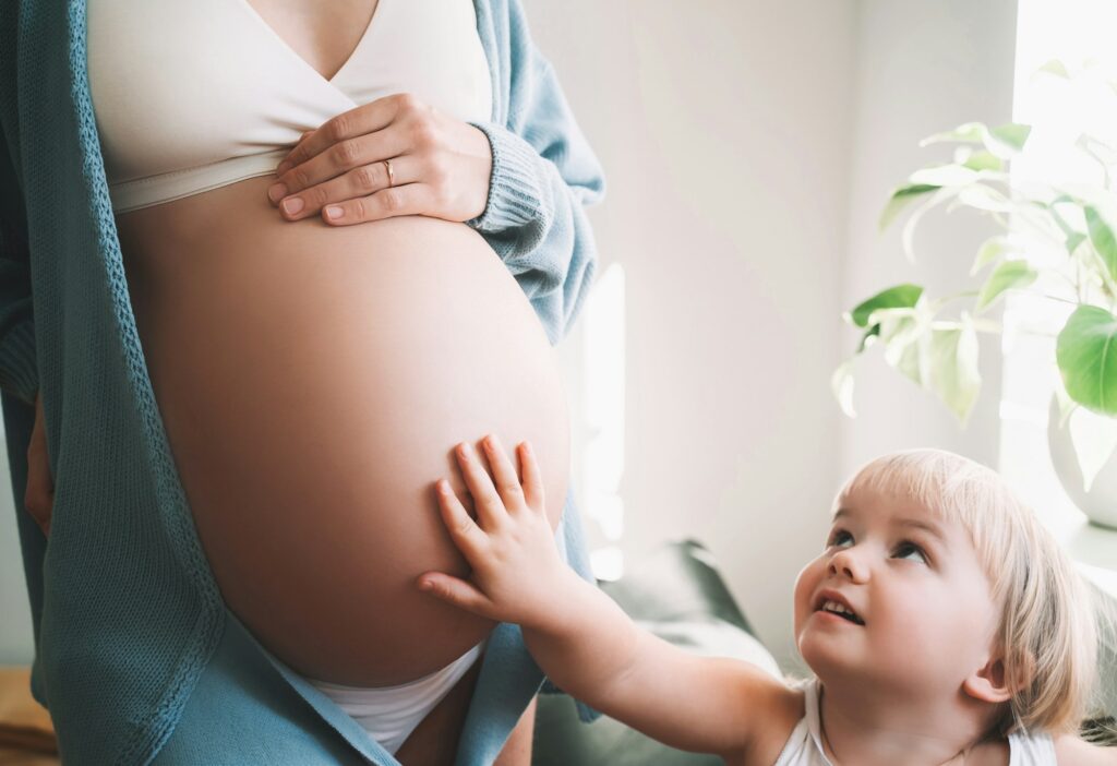 Little girl put her hand on belly of pregnant mother. Pregnant woman and child.